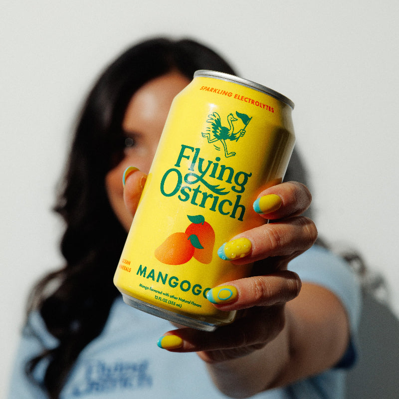 Person holding a can of 'Flying Ostrich Mango' drink against a plain background