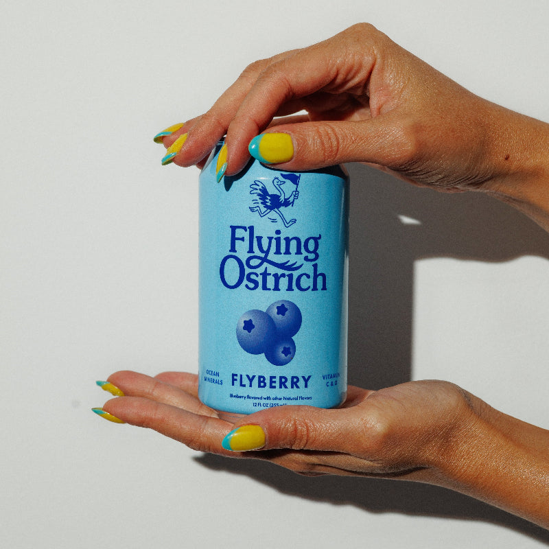 Hand holding a can of Flying Ostrich Flyberry drink against a plain background